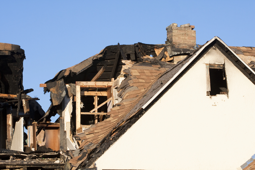 A house with severe fire damage; parts of the roof and upper structure are charred and partially collapsed, exposing interior wooden beams—ideal for a water damage restoration service to assess and restore.